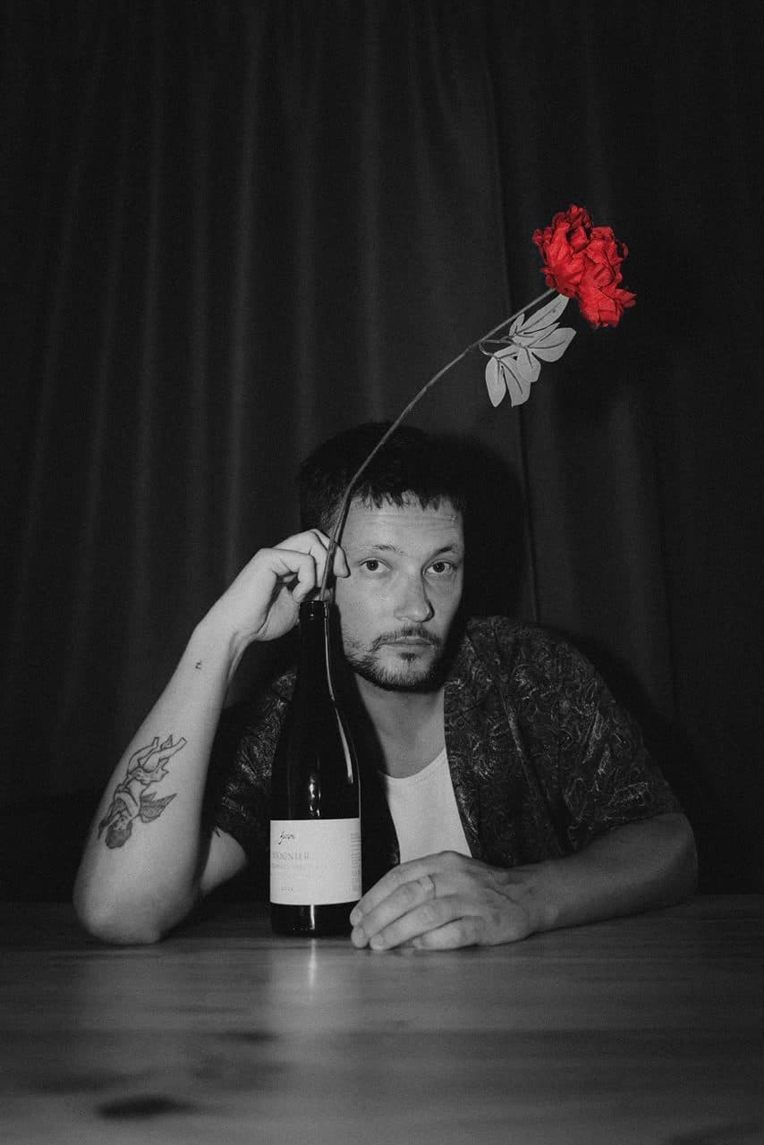 Tyan in a black and white portrait with a single red rose in the foreground.